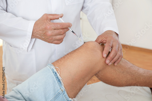 Doctor giving patient injection in clinic  closeup. Knee problem treatment