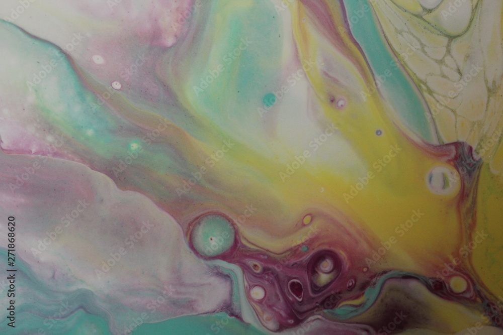 Closeup on an abstract acrylic pour painting that is done in yellow, teal, magenta, purple and white that resembles the aurora borealis.