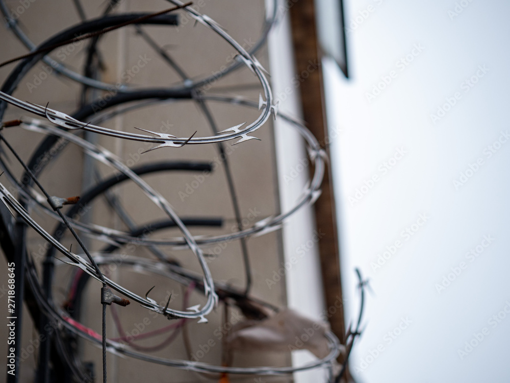 Close view of barbed wire razor wire on top of fence outside of a building in overcast Close view of barbed wire razor wire on top of fence outside of a building in overcast