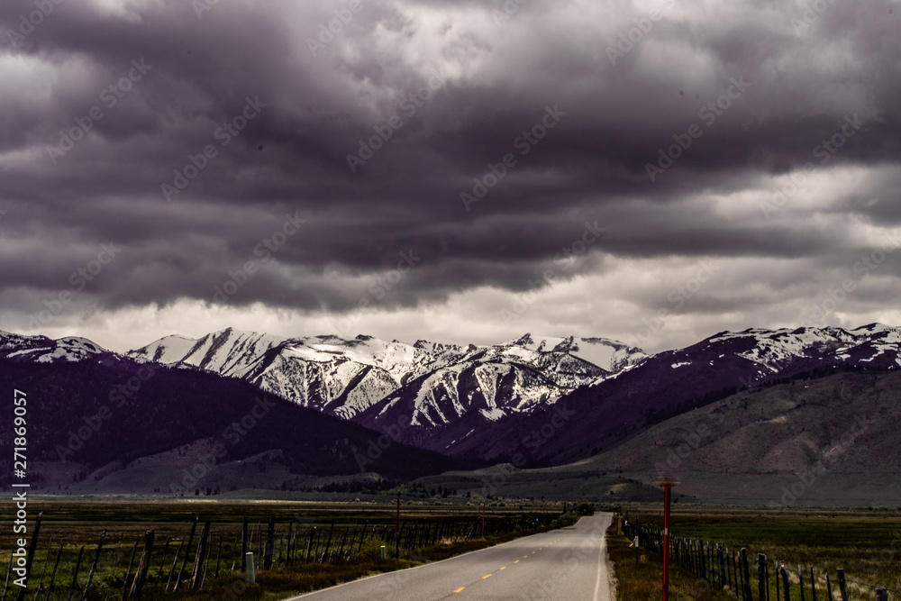 View of snow capped Eastern Sierra Nevada Mountains with white and grey clouds, blue sky, green meadows and hills