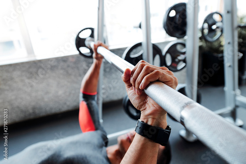 Hands of athlete doing exercise with heavy barbell on gym bench