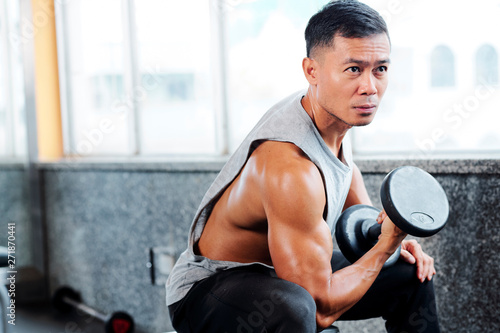 Handsome fit Asian man lifting weights in gym on arm day