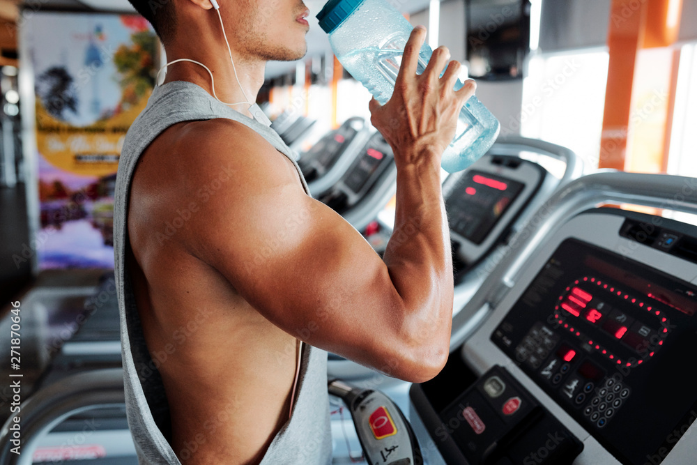 Cropped image of strong fit man standing on treadmill with big water bottle in hands Cropped image of strong fit man standing on treadmill with big water bottle in hands