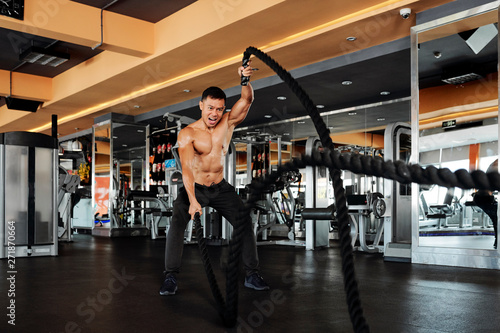 Shirtless Vietnamese sportsman shouting when doing exercise with battle ropes