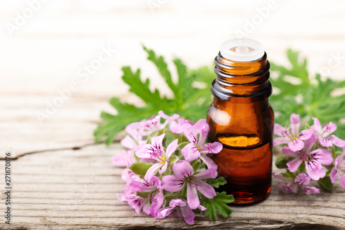 Geranium essential oil with fresh geranium flowers, on the old wooden board