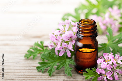 Geranium essential oil with fresh geranium flowers, on the old wooden board photo