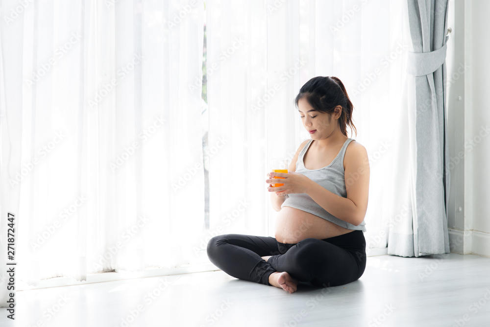 Asian pregnant woman holding a glass of orange juice and sitting near window, lifestyle concept. Asian pregnant woman holding a glass of orange juice and sitting near window, lifestyle concept.