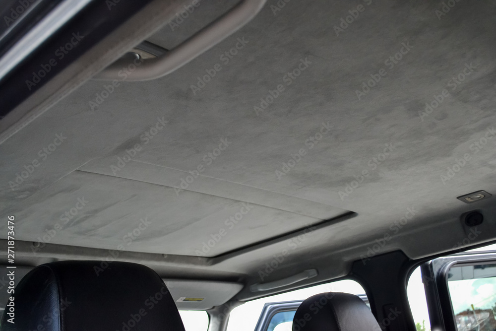 The ceiling of the SUV car with sunroof pulled by gray soft material in the workshop for tuning and styling the interior of the vehicles with sunroof. Auto service industry.