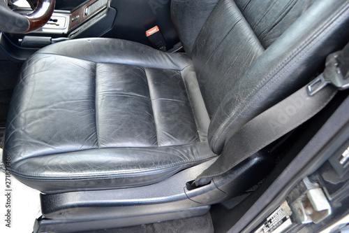 Close-up on the front old classic car seat with black leather trim, of used vehicle in bad condition in the interior after detailing and dry cleaning. Auto service industry.
