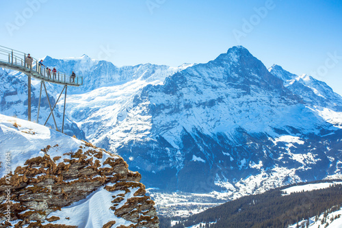 Tourists are standing on and seeing the scenery from a terrace located at the First summit. Visible in a distance is the Eiger, a mountain in the Swiss Alps Jungfrau-Aletsch World Heritage sites.