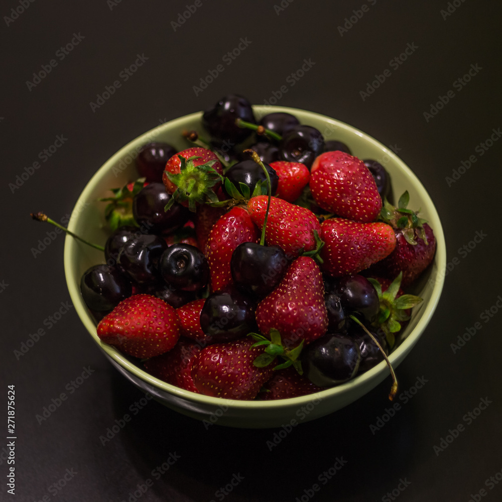 Fresh fruit of strawberries and cherries in a cup on a dark background. Fresh fruit of strawberries and cherries in a cup on a dark background.