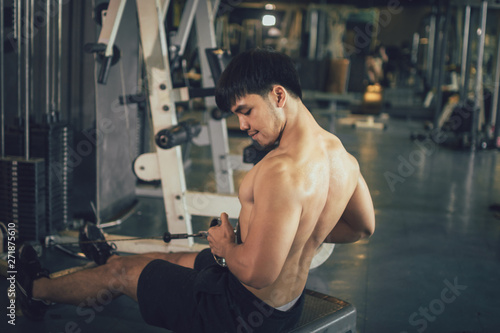 Asian sportsman pull still weight for building muscle at indoor gym.