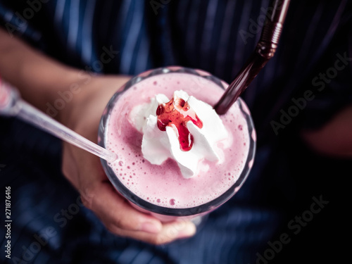Fototapeta Naklejka Na Ścianę i Meble -  Close-up hand of Asian young women sitting on the chair at outside of the coffee cafe and holding strawberry smoothie in clear glass.