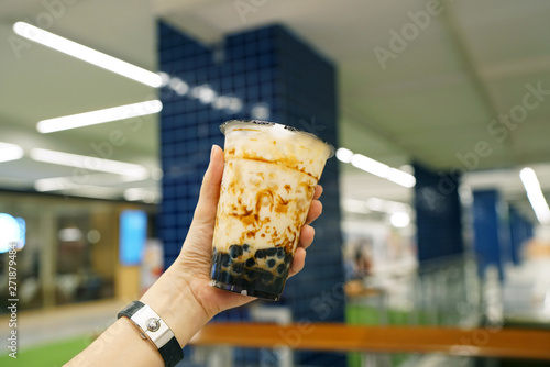 Bubble Milk Tea - Holding a plastic glass of fresh milk with black sugar syrup (Kuromitsu) and hot black pearl (Boba) on blurred background, Taiwanese style. photo