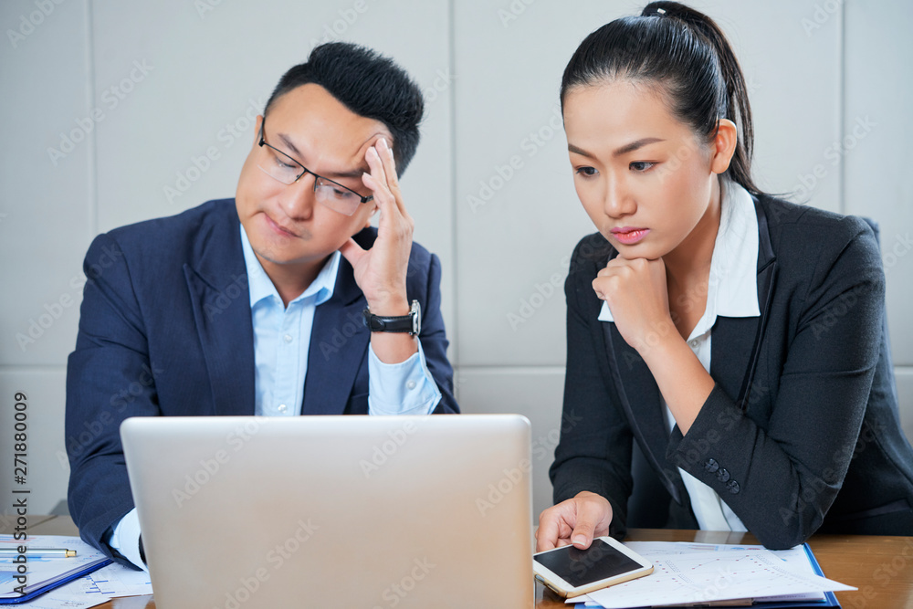 Concerned Vietnamese business colleagues reading e-mail with bad news on laptop screen Concerned Vietnamese business colleagues reading e-mail with bad news on laptop screen