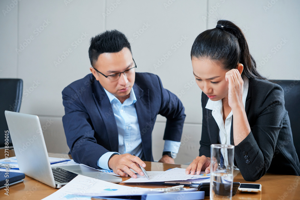 Serious businessman pointing at mistake of female coworker in financial report Serious businessman pointing at mistake of female coworker in financial report