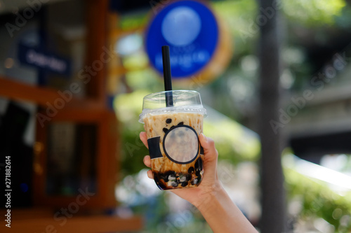 Hand Holding a plastic glass of refreshing Milk Tea Latte with bubble (boba), selective focus. blue background 