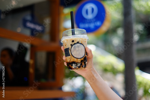 Hand holding a plastic glass of milk iced tea mixed with brown sugar with bubble (boba). selective focus.