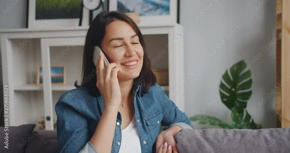 Slow motion of young woman talking on mobile phone and smiling at home enjoying modern communication with friends. Happy youth, flat and lifestyle concept. Slow motion of young woman talking on mobile phone and smiling at home enjoying modern communication with friends. Happy youth, flat and lifestyle concept.