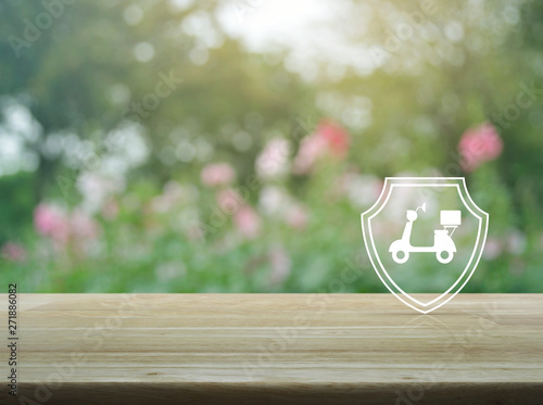 Motorcycle with shield flat icon on wooden table over blur pink flower and tree in garden, Business motorbike insurance concept
