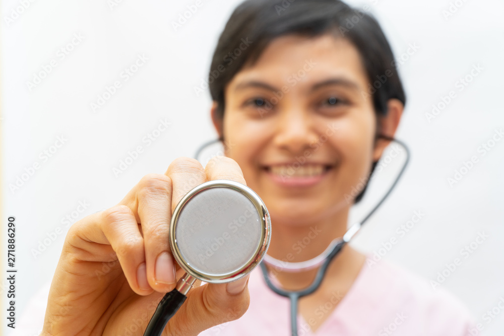 Asian short hair female medical doctor holding stethoscope, checking heart beat and smiling. She is standing while looking at camera in hospital,health care concept. Blurry face and space for text Asian short hair female medical doctor holding stethoscope, checking heart beat and smiling. She is standing while looking at camera in hospital,health care concept. Blurry face and space for text