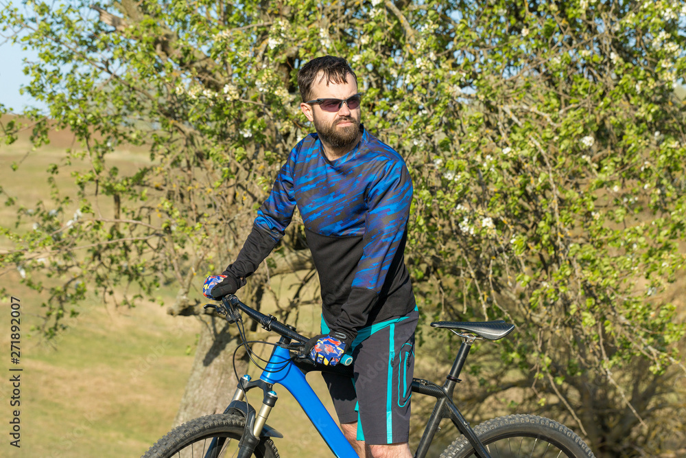 Fototapeta premium Cyclist in shorts and jersey on a modern carbon hardtail bike with an air suspension fork rides off-road on green hills near the forest 