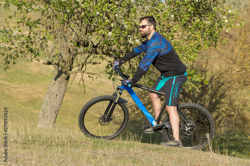 Cyclist in shorts and jersey on a modern carbon hardtail bike with an air suspension fork rides off-road on green hills near the forest Cyclist in shorts and jersey on a modern carbon hardtail bike with an air suspension fork rides off-road on green hills near the forest