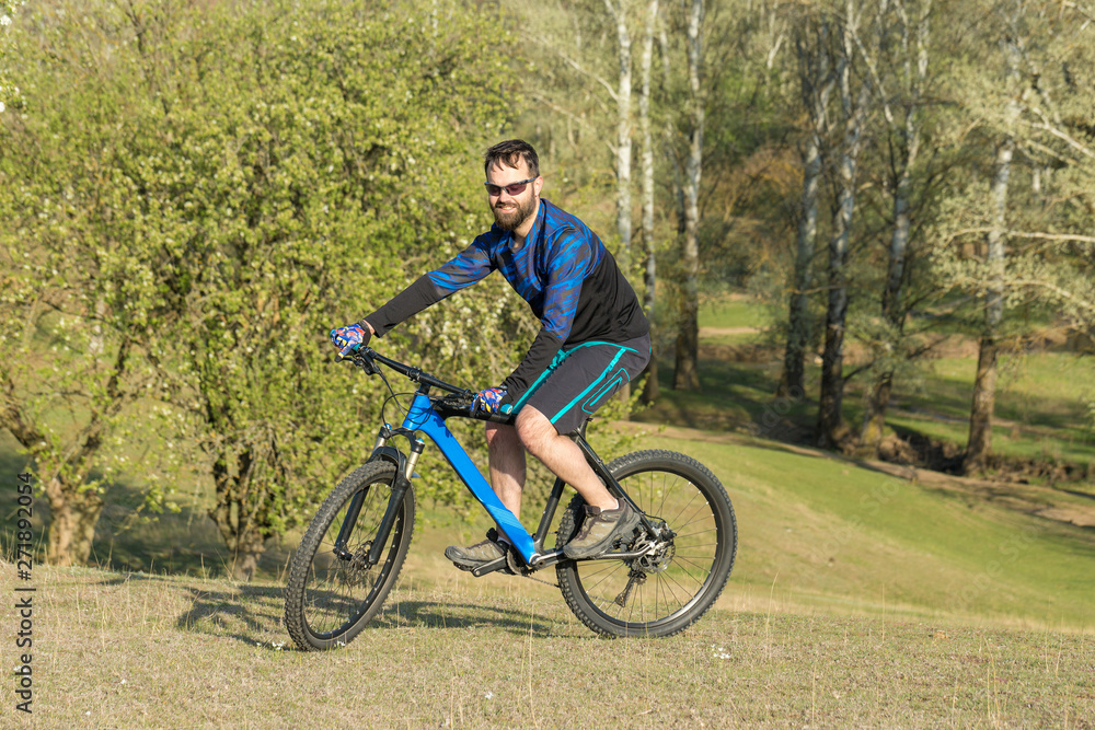 Cyclist in shorts and jersey on a modern carbon hardtail bike with an air suspension fork rides off-road on green hills near the forest Cyclist in shorts and jersey on a modern carbon hardtail bike with an air suspension fork rides off-road on green hills near the forest