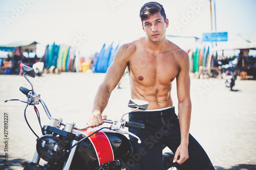 handsome sexy sporty young man with a naked fit torso sitting on custom motorcycle with sunlight background