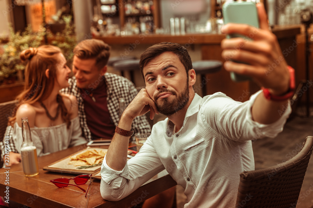 Obraz premium Upset man selfies while his friends hugging at the background.