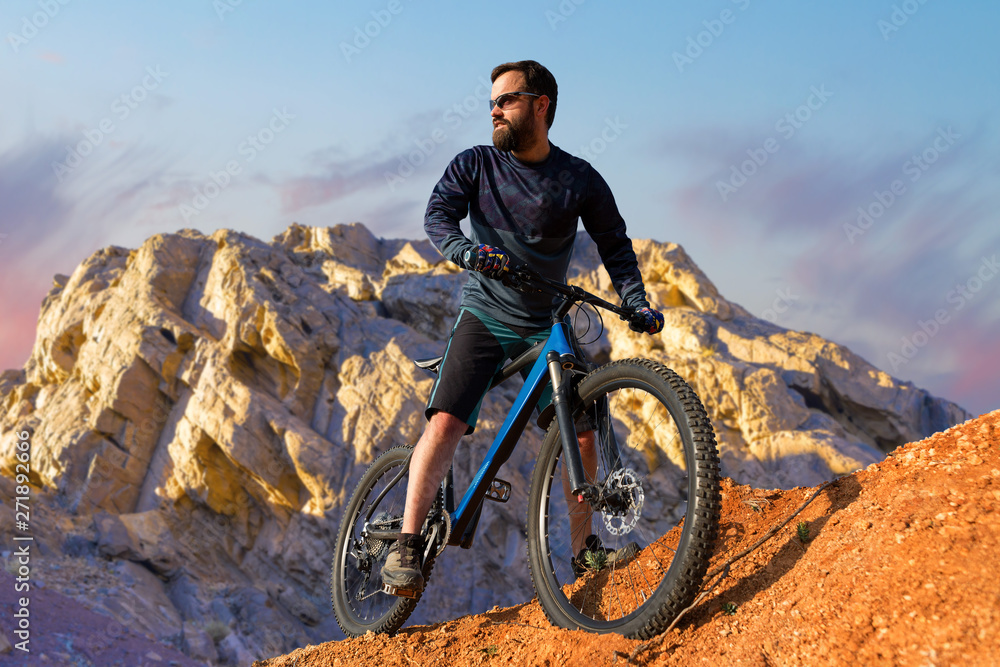 Fototapeta premium Cyclist in shorts and jersey on a modern carbon hardtail bike with an air suspension fork rides off-road on the orange-red hills at sunset evening in summer 