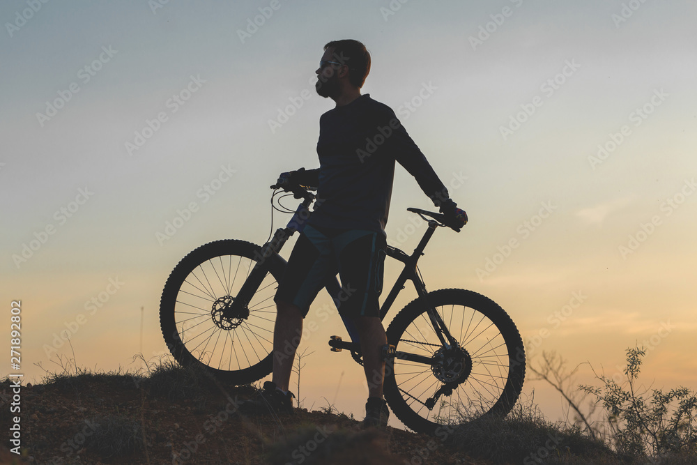 Cyclist in shorts and jersey on a modern carbon hardtail bike with an air suspension fork rides off-road on the orange-red hills at sunset evening in summer Cyclist in shorts and jersey on a modern carbon hardtail bike with an air suspension fork rides off-road on the orange-red hills at sunset evening in summer