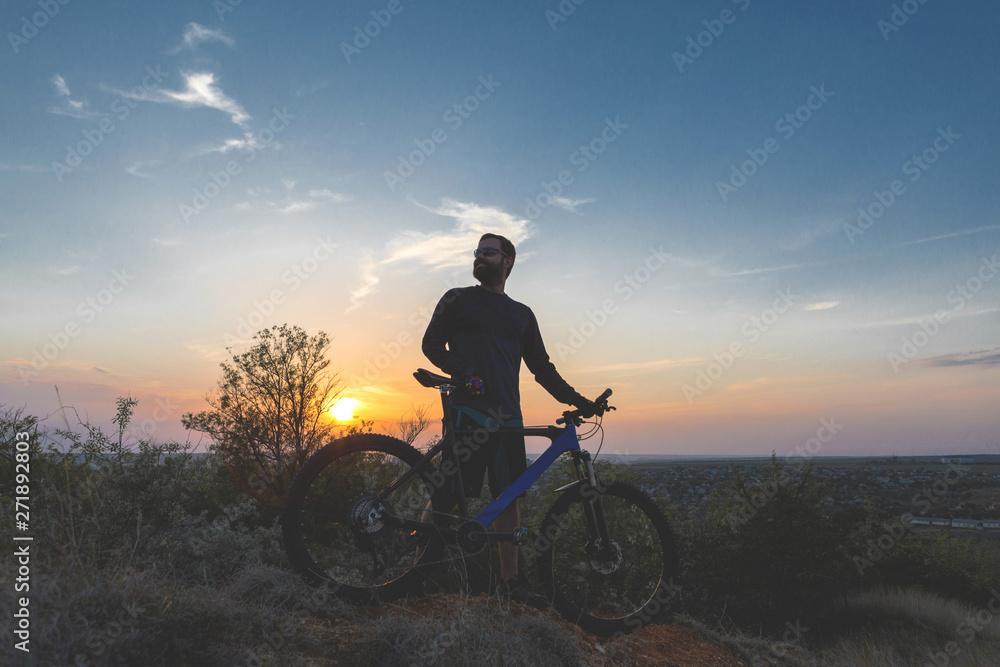 Cyclist in shorts and jersey on a modern carbon hardtail bike with an air suspension fork rides off-road on the orange-red hills at sunset evening in summer Cyclist in shorts and jersey on a modern carbon hardtail bike with an air suspension fork rides off-road on the orange-red hills at sunset evening in summer