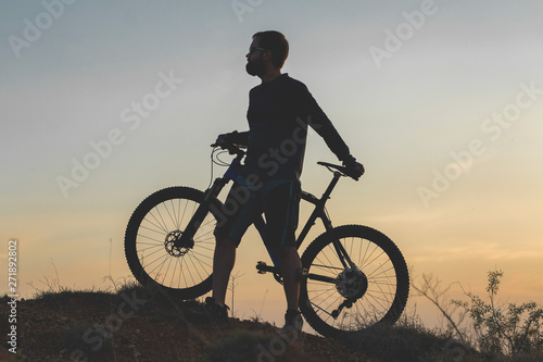 Cyclist in shorts and jersey on a modern carbon hardtail bike with an air suspension fork rides off-road on the orange-red hills at sunset evening in summer 