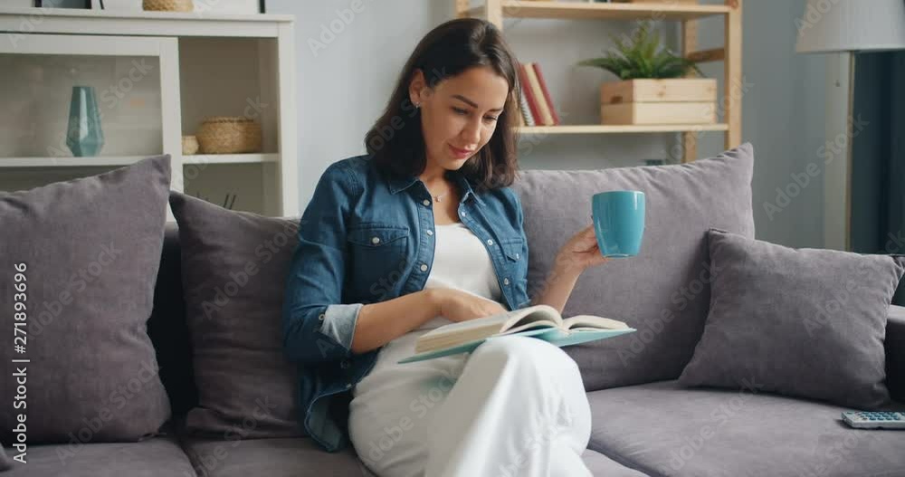 Cute student attractive young woman is reading book and drinking coffee relaxing at home on sofa. Youth culture, lifestyle and happy millennials concept. Cute student attractive young woman is reading book and drinking coffee relaxing at home on sofa. Youth culture, lifestyle and happy millennials concept.