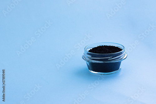 Dry raw sweet black basil seeds, other name tukhmaria or falooda or sabja in glass bowl on blue background with copy space. Trendy ingredient for making healthy food, beverages, vegan and dietary photo