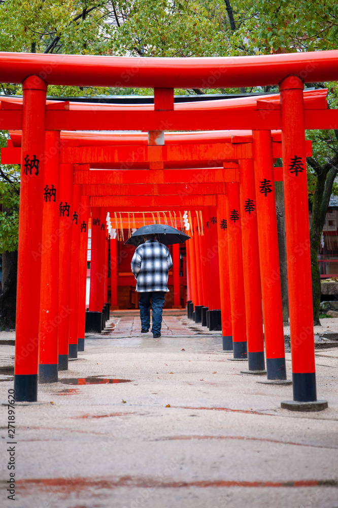 神社の雨に濡れた赤い建築物を歩く人