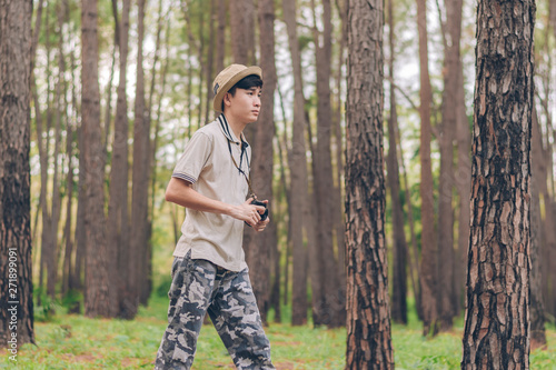 Asia man wears shirt, hat, and camouflage pants are walking and taking photos at the forest. © Palakorn Jaiman