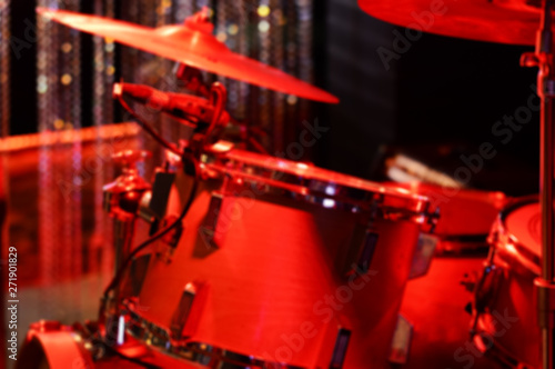 blurred background with acoustic drum set and cymbals on club stage in red lights