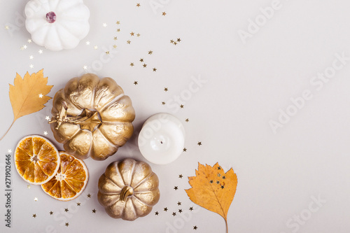 Autumn Celebration concept. Decorative pumpkins  golden confetti and dry leaves on gray background