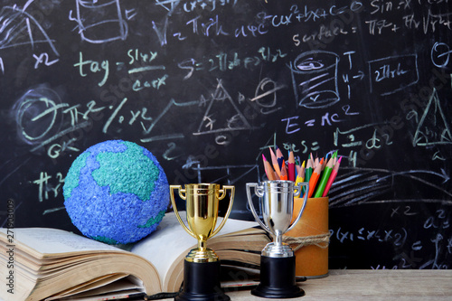 Study learning achievement success in abroad education global ideas: School books with global model on open book, gold silver trophy on desk,pencils box, formula math equation blackboard background