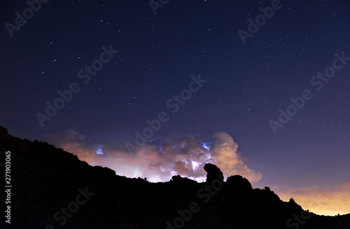 Rays and clouds in night storm over the mountain under a starry sky