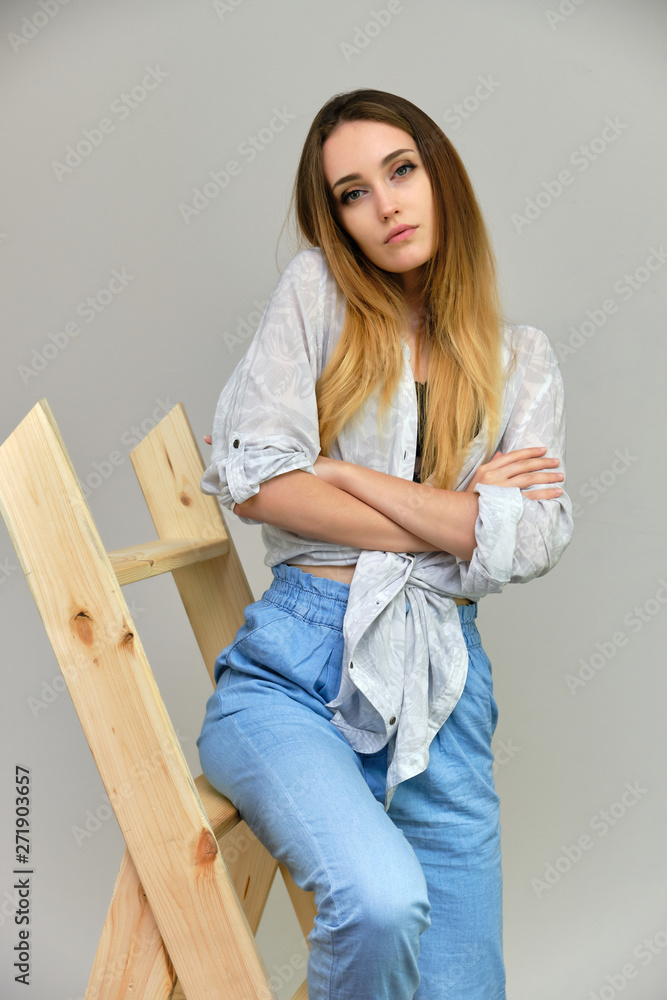 Photograph of a portrait of a beautiful girl woman with long dark flowing hair, fashionable, on a gray background sitting on a wooden staircase. She sits in different poses and smiles.