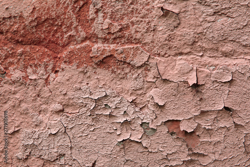 Fragment of an old exterior wall with cracked peeling plaster pink color