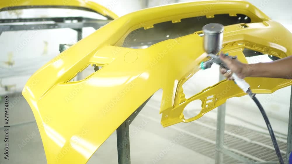 Man with protective clothes and mask painting car using spray compressor ,yellow front bumper Man with protective clothes and mask painting car using spray compressor ,yellow front bumper
