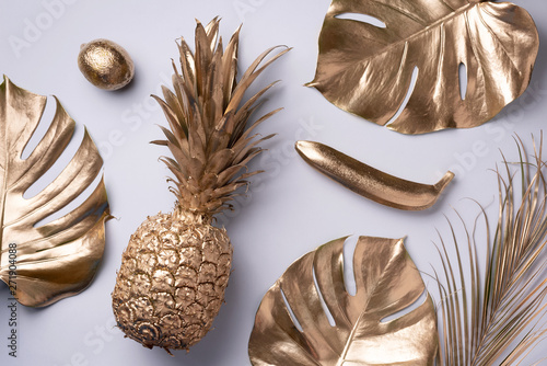 Creative layout. Gold pineapple and golden palm, monstera on grey background with copy space. Top view. Tropical flat lay. Exotic food concept, crazy trend. Banner photo