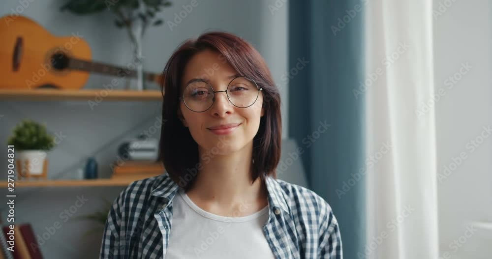 Slow motion portrait of cheerful girl turning head looking at camera smiling wearing glasses and casual clothing. People, apartment and youth concept. Slow motion portrait of cheerful girl turning head looking at camera smiling wearing glasses and casual clothing. People, apartment and youth concept.