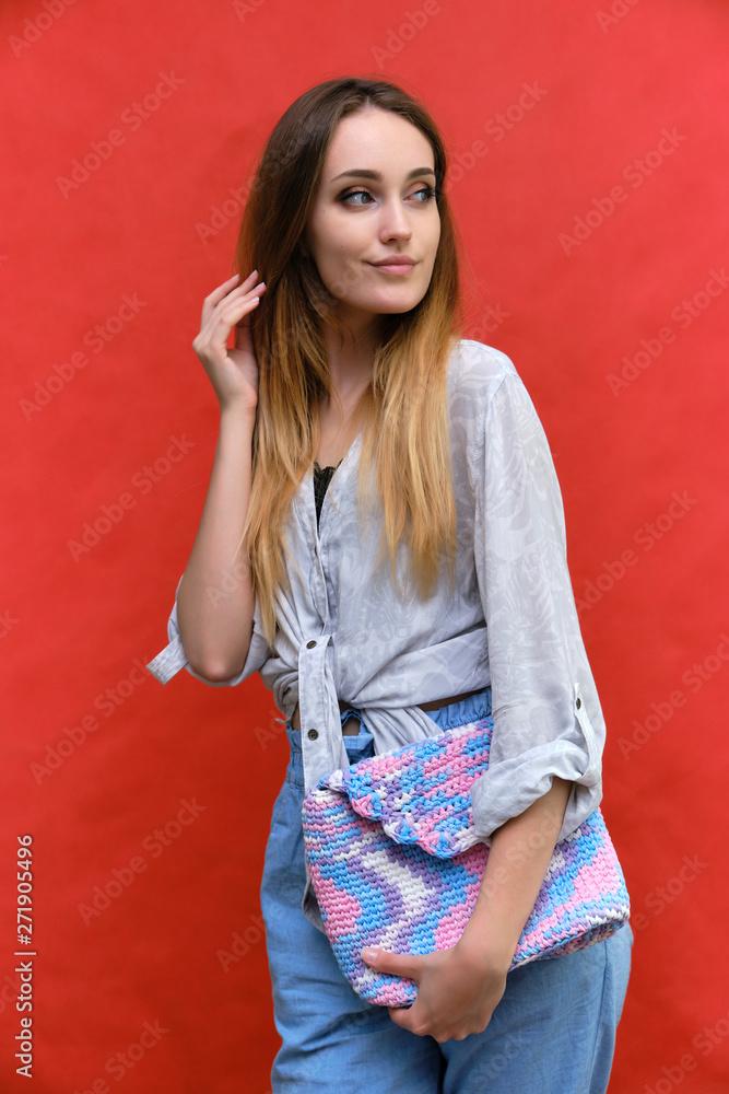 Photograph of a portrait of a beautiful fashionable beauty woman girl with long dark flowing hair, on a red background with a bag. She is standing in different poses and smiling. Photograph of a portrait of a beautiful fashionable beauty woman girl with long dark flowing hair, on a red background with a bag. She is standing in different poses and smiling.