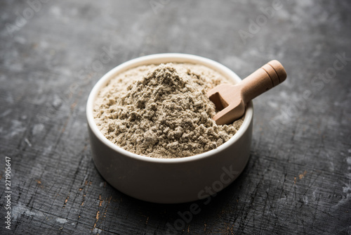 bajra atta / flour of pearl millet served in a bowl with small wooden scoop, selective focus