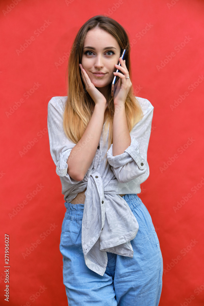 Photograph of a portrait of a beautiful fashionable beauty girl woman with long dark flowing hair, on a red background with a smartphone. She is standing in different poses and smiling. Photograph of a portrait of a beautiful fashionable beauty girl woman with long dark flowing hair, on a red background with a smartphone. She is standing in different poses and smiling.